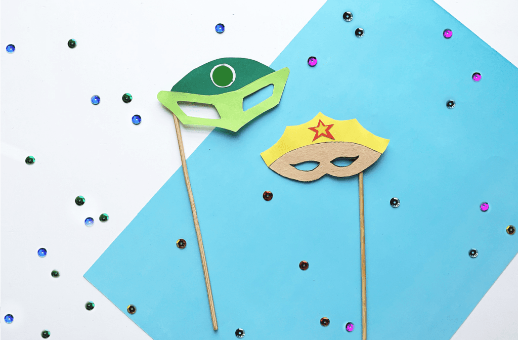 green superhero mask and yellow crown mask on sticks with blue background and sequins