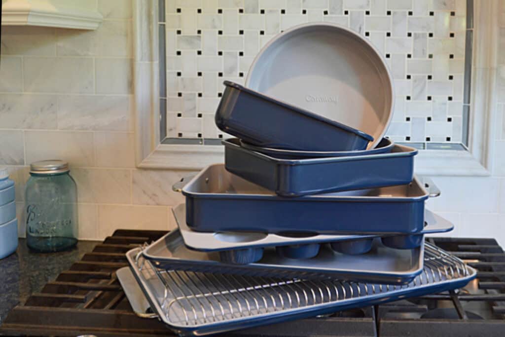 navy blue Caraway ceramic baking pans stacked on stove top in front of marble backsplash