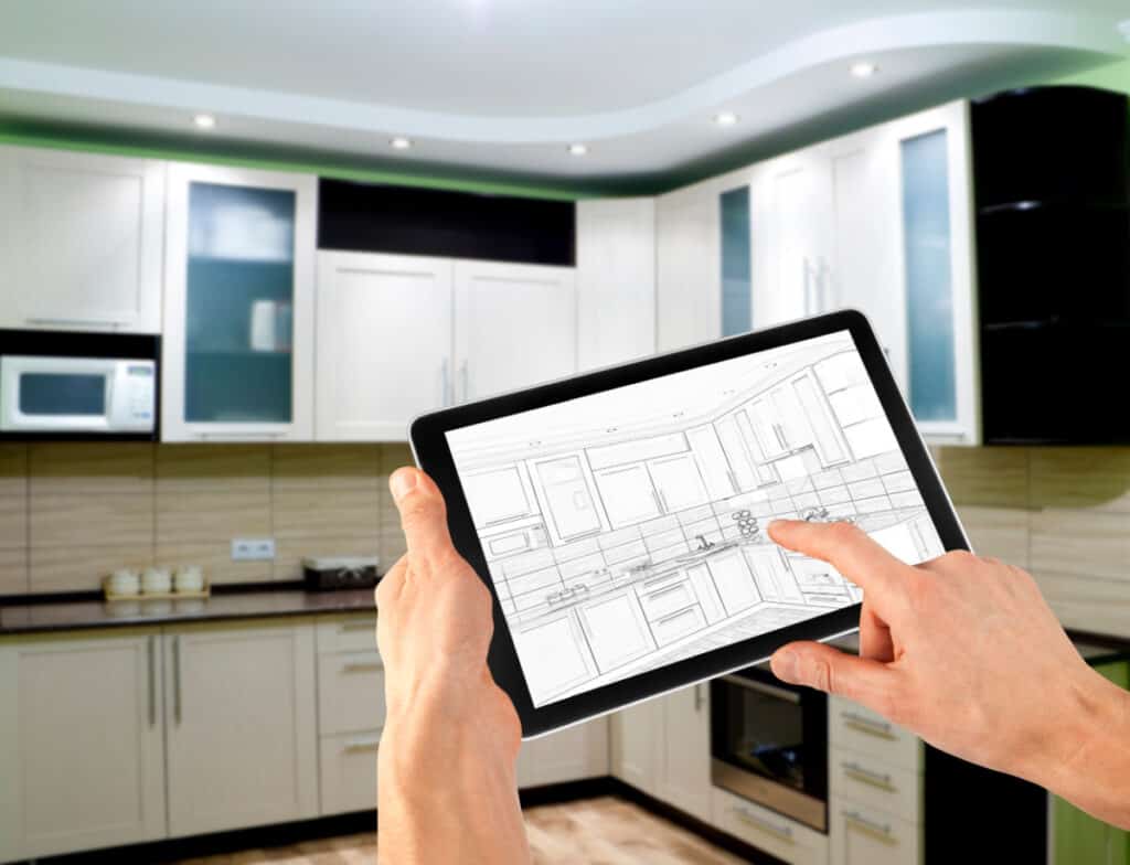 hands holding tablet with kitchen drawing in front of actual kitchen.