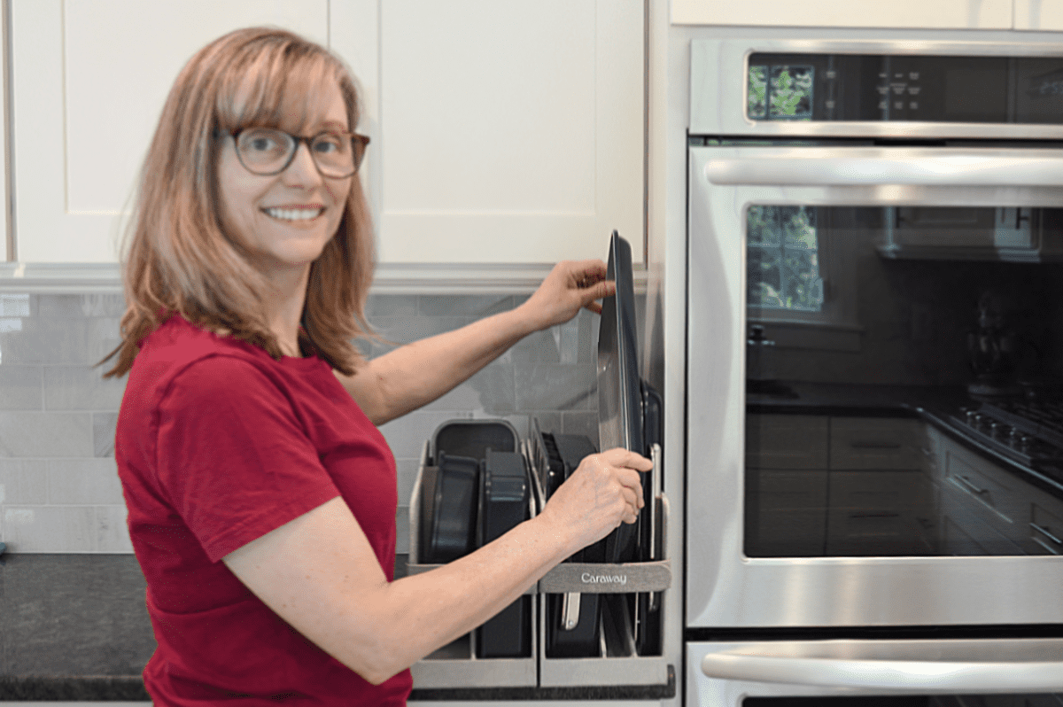 blonde woman in red shirt placing baking pan in organizing bin next to oven