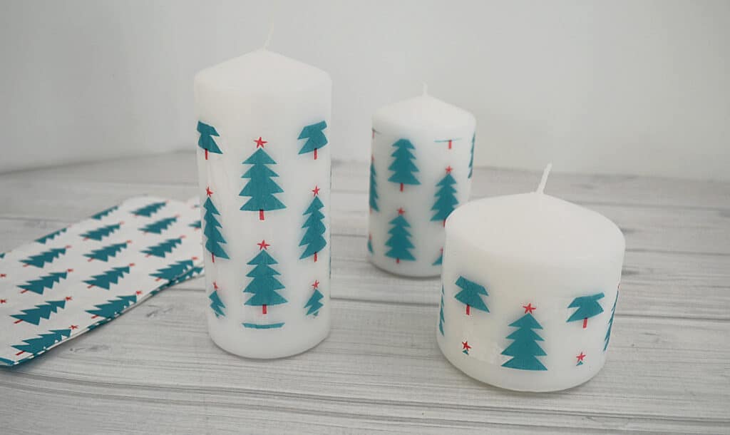 3 white candles with green tree with red star with paper napkins with same design.