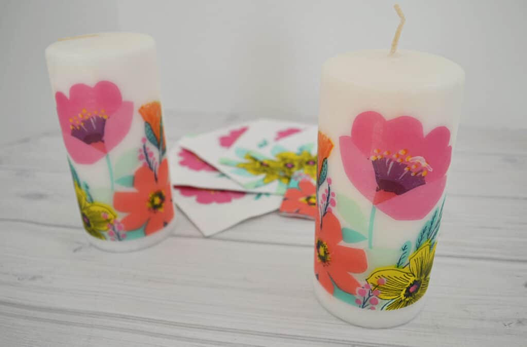 close up of 2 floral candles with floral napkins on white wood table.