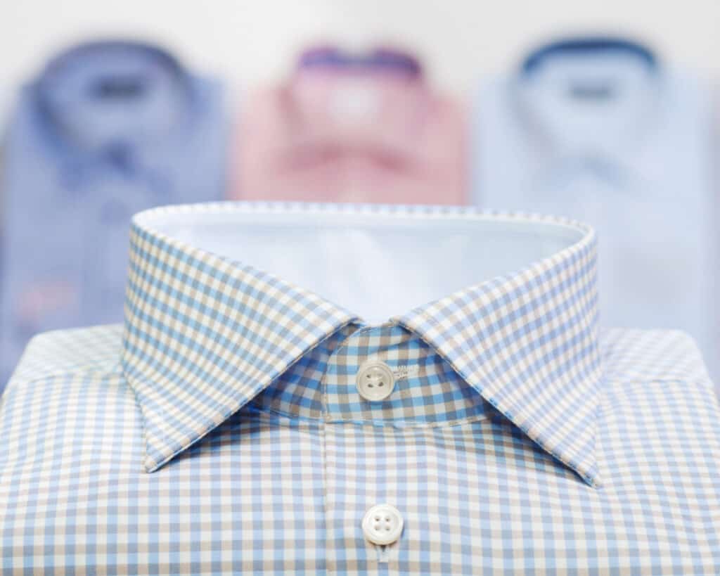 close up of light green and white dress shirt collar with 3 more folded dress shirts in background.