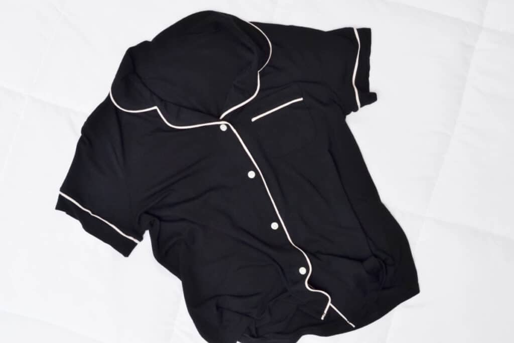 overhead view of black pajama top with white buttons and piping on white comforter.