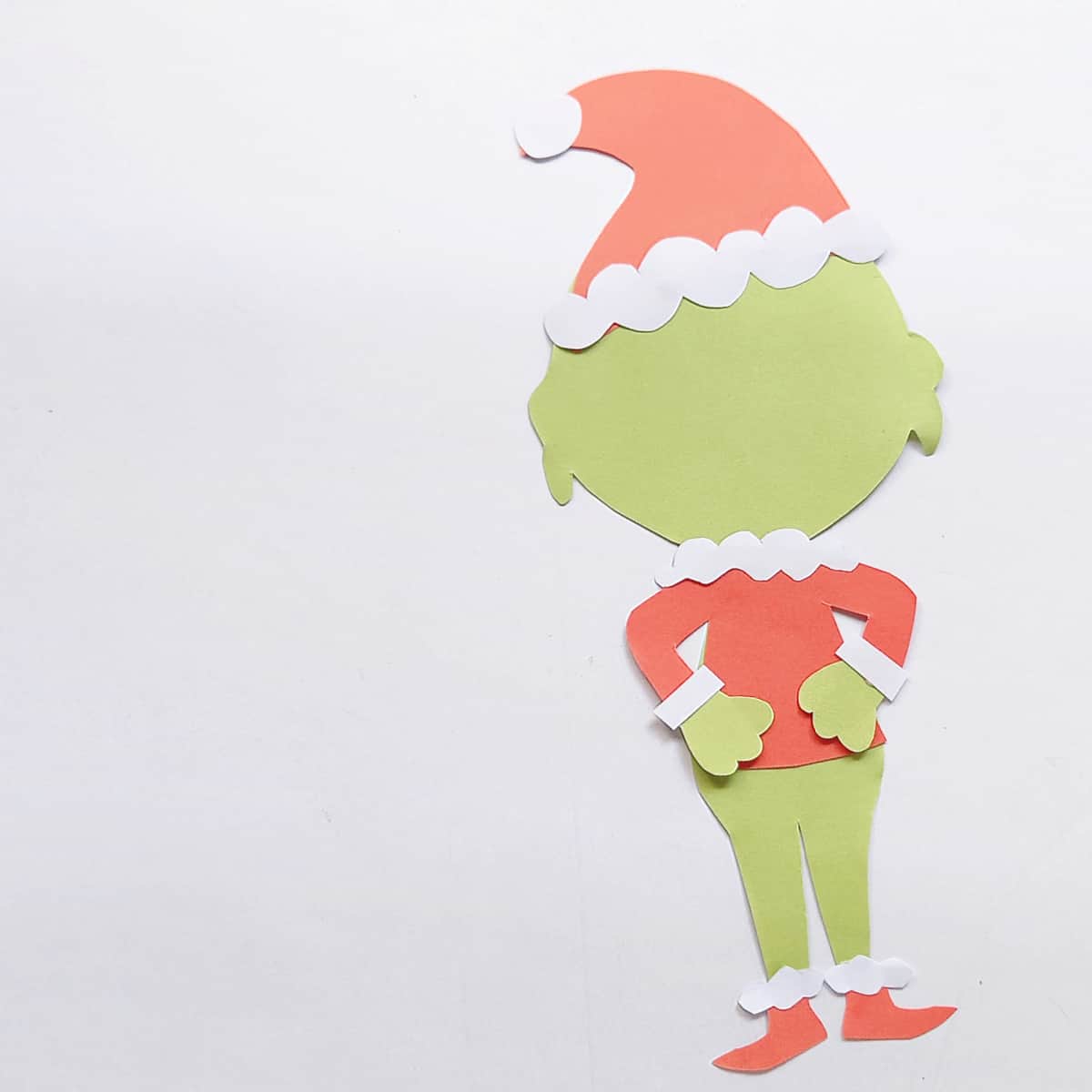 Grinch paper craft with green body, red hat, red coat and red shoes with white trim.