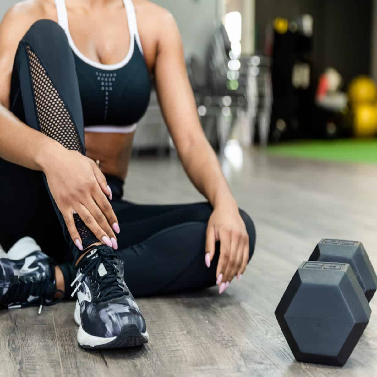 A woman sitting on the floor in a gym with dumbbells.
