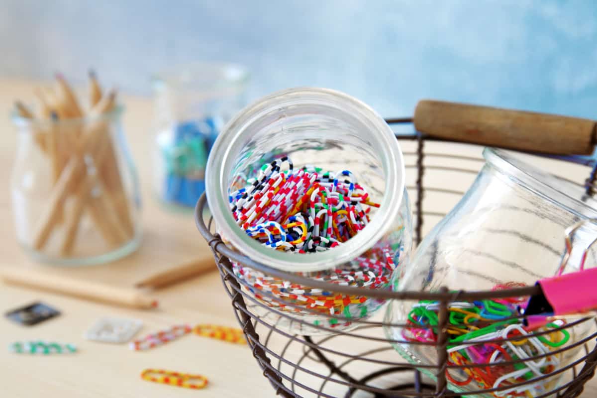 A metal basket filled with paper clips and pencils in jars.